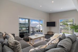 A modern living room with a grey sofa, a coffee table, and a flat-screen TV mounted on the wall. - Wharf Landing: The Apartment (Coromandel)