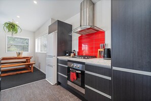 A modern kitchen with dark cabinetry, a red backsplash, a gas stove, and a built-in oven. - Wharf Landing: The Apartment (Coromandel)