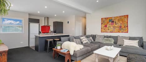 A modern living room with a grey sofa, a coffee table, and a kitchen area in the background.