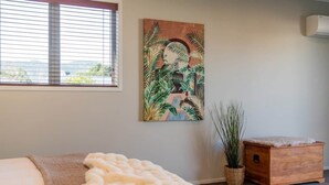 A bedroom with a bed, a large window, a painting, a plant, and a wooden chest. - Wharf Landing: The Studio (Coromandel)