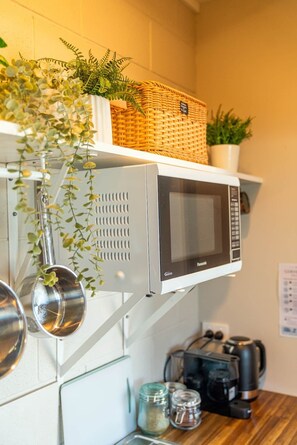 A kitchen with a microwave, hanging pots, a coffee maker, and a shelf with plants. - Wharf Landing: The Studio (Coromandel)