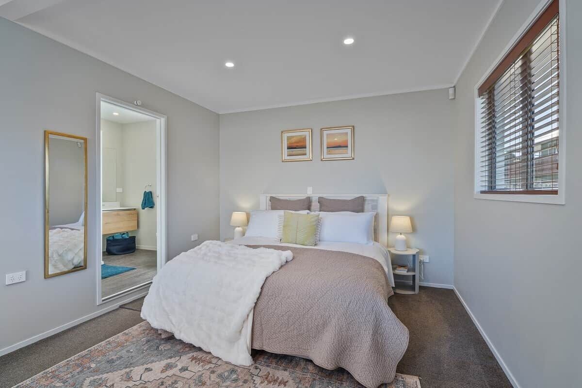 A bedroom with a bed, bedside lamps, a mirror, and a window with blinds.