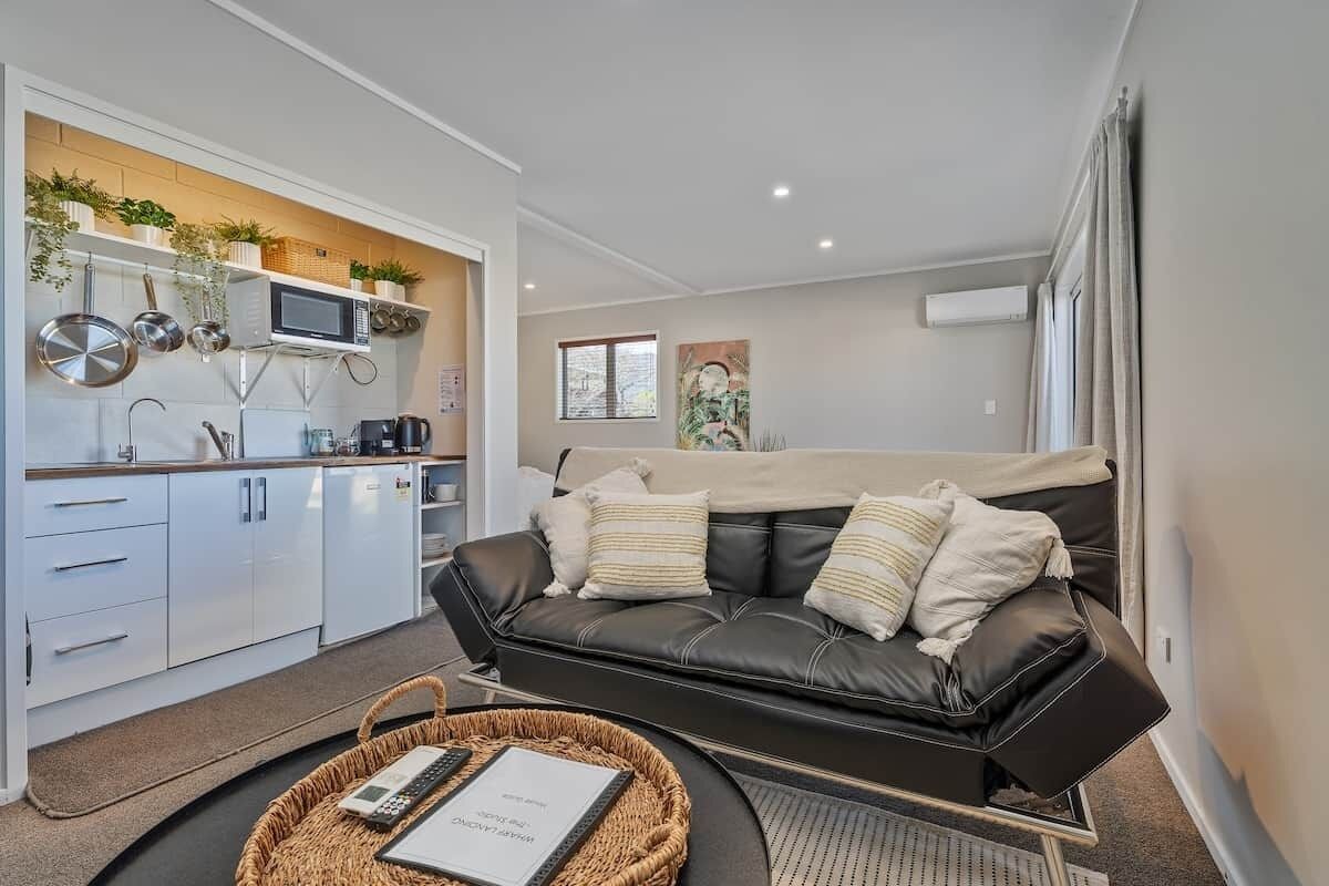 A compact living space with a kitchenette, a black leather sofa, and a small dining table.