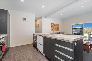 A modern kitchen with a central island, built-in appliances, and a large window providing natural light. - Wharf Landing: Entire Home (Coromandel)
