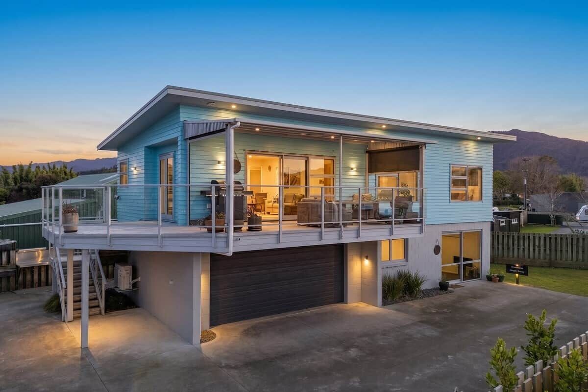 A modern two-story house with a covered patio, garage, and a view of mountains in the background.