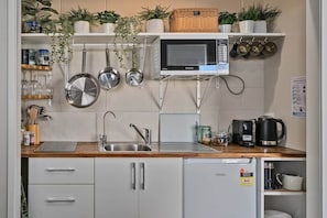 Eine kompakte Küche mit Mikrowelle, Wasserkocher und Kaffeemaschine. Regale mit Pflanzen und Küchenutensilien sind vorhanden.