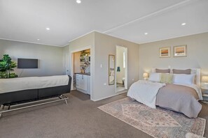 Ein Schlafzimmer mit einem Bett, einem Schreibtisch, einem Sessel, einem Fernseher und einem durch eine offene Tür einsehbarer Badezimmer.