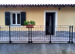 A building with a yellow facade, a black metal fence, a potted plant, and a door.