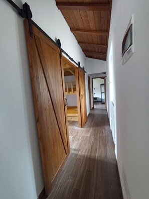 A hallway with wooden flooring, a sliding barn door, and a view into a room with a bed and a window.