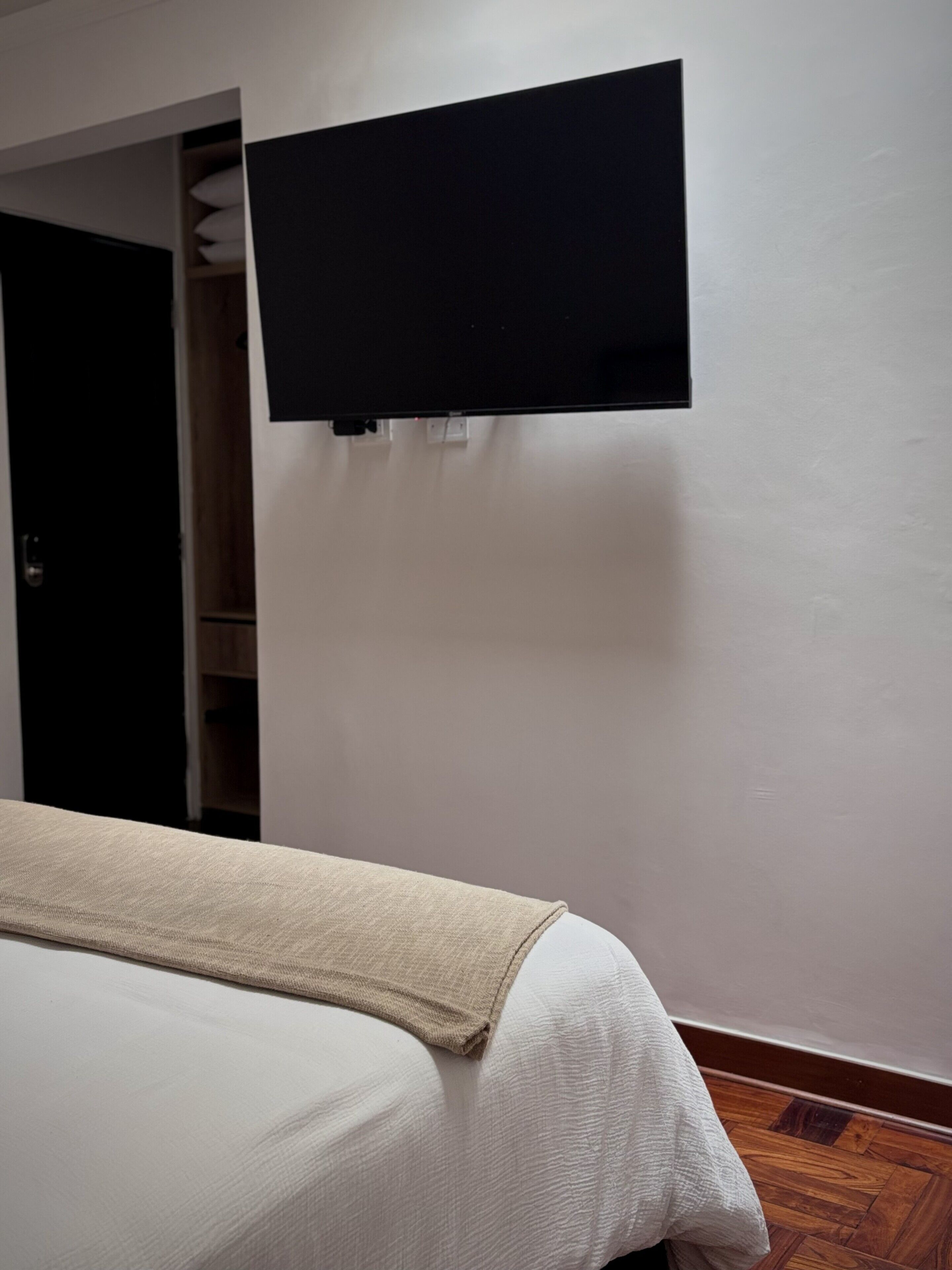 Un dormitorio con una cama, un armario y un televisor montado en la pared.