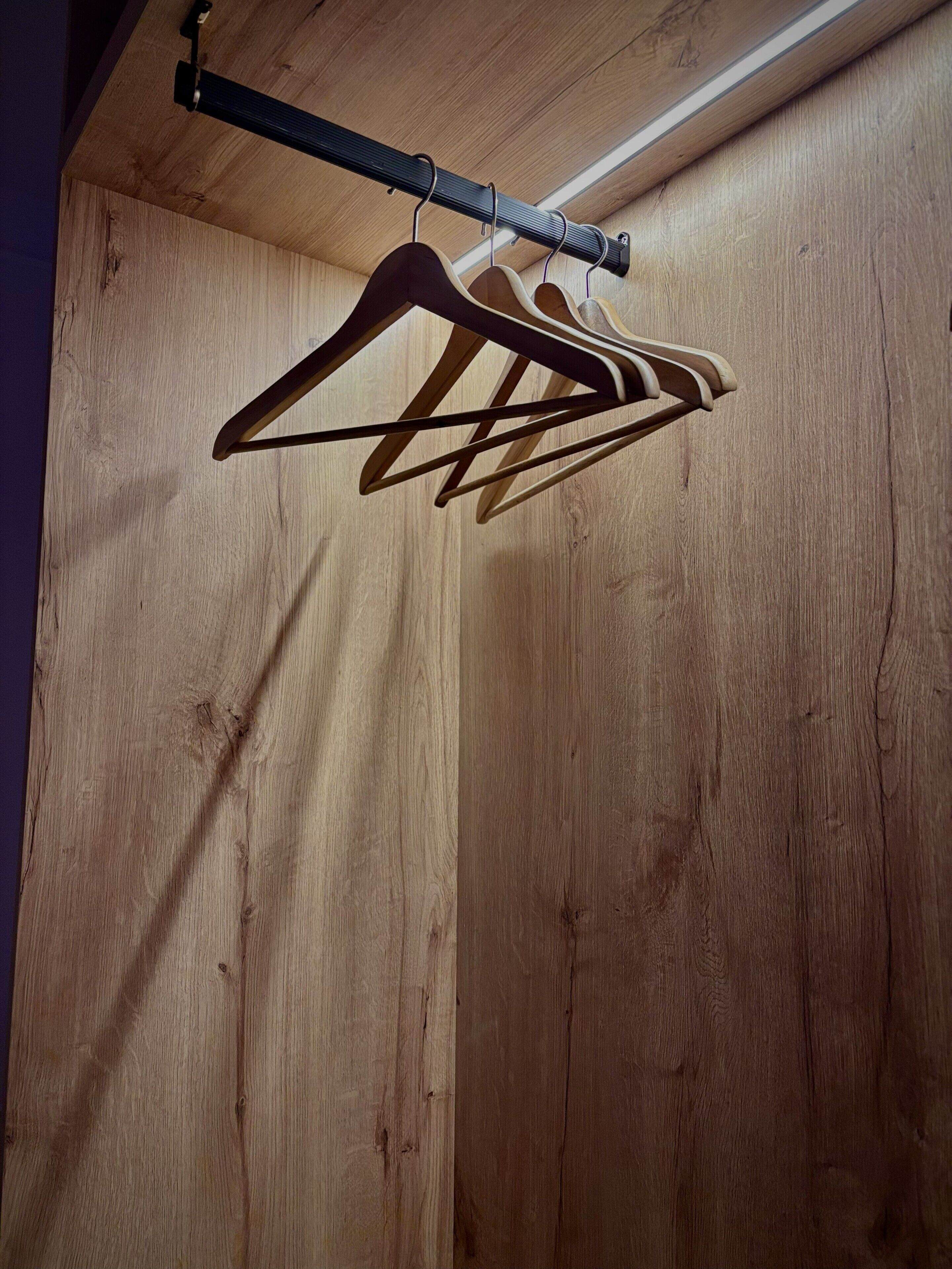 Pared de madera con una barra de metal negro y perchas de madera.
