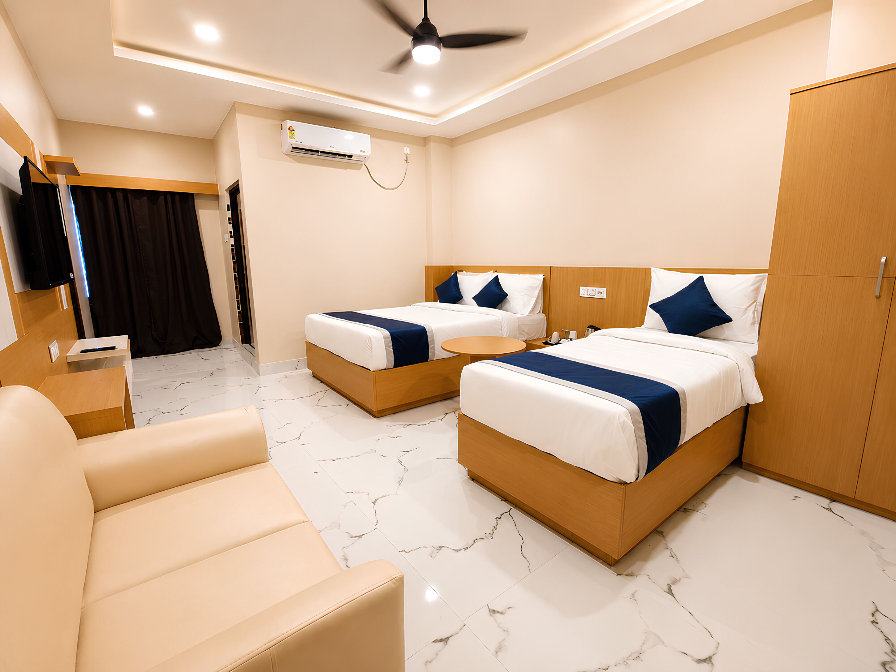 A hotel room with two beds, a sofa, a desk, and an air conditioning unit.