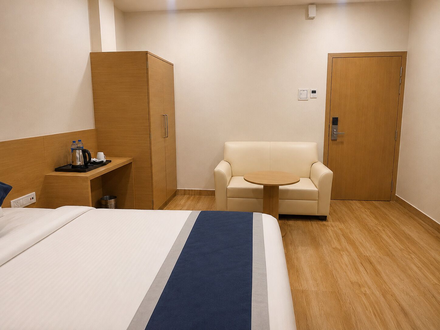 A hotel room with a bed, a desk with a coffee maker, a chair, and a wardrobe.