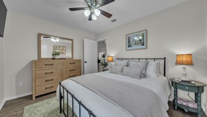 A bedroom with a bed, dresser, nightstand, lamp, ceiling fan, and artwork.