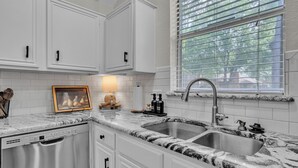A kitchen with white cabinets, a granite countertop, a stainless steel sink, and a window with blinds.