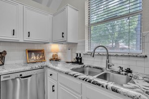 A kitchen with white cabinets, a granite countertop, a stainless steel sink, and a window with blinds.