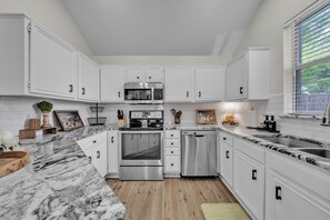 Una cucina moderna con mobili bianchi, un forno in acciaio inossidabile, una lavastoviglie e un piano di lavoro in marmo.