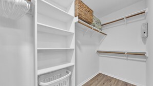A white interior with a wooden floor, a white laundry basket, and a shelf with a woven basket.