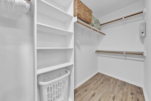 A white interior with a wooden floor, a white laundry basket, and a shelf with a woven basket.