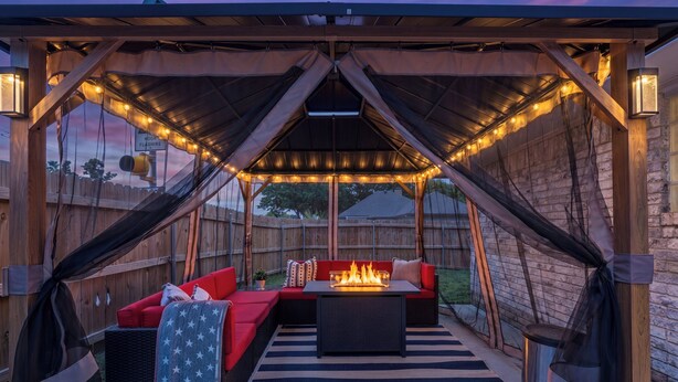 An outdoor patio with a covered seating area, a fire feature, and string lights.