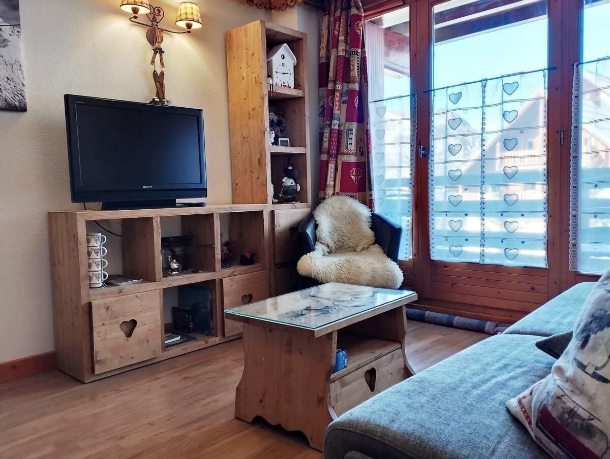A cozy living room with a wooden TV stand, a fluffy chair, and a small table.