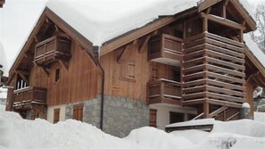 Eine Holzhütte mit steinernem Fundament, Balkonen und einem Schild mit der Aufschrift 'CHLET C'.