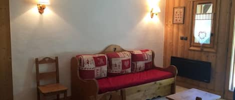 Une pièce chaleureuse avec un canapé en bois, une chaise en bois, une petite table et deux lampes fixées au mur.