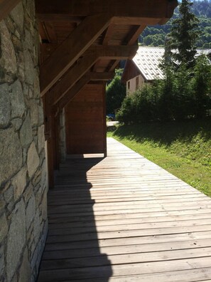 Eine Holzterrasse führt zu einem Steinhaus mit Satteldach.