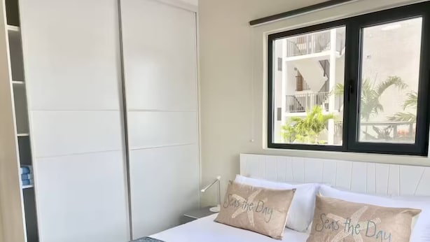Ein Schlafzimmer mit einem Bett, Kissen, einem Fenster und Blick auf ein Gebäude.