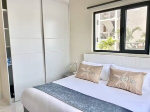 A bedroom with a bed, pillows, a window, and a view of a building outside. - Grace Bay Hideaway. 1 bedroom, central Grace Bay. (Grace Bay)