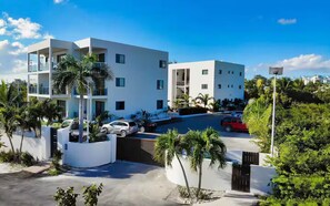 A modern multi-story building with a parking area, surrounded by palm trees and greenery. - Grace Bay Hideaway. 1 bedroom, central Grace Bay. (Grace Bay)