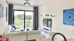 Ein modernes Wohnzimmer mit einer Couch, einem Flachbildfernseher und Blick auf einen Garten durch eine Schiebetür.