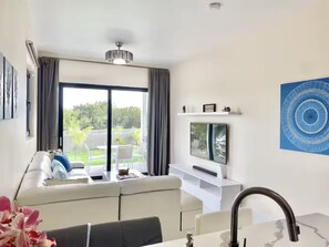 A modern living room with a sofa, a flat-screen TV, and a view of a garden through a sliding door. - Grace Bay Hideaway. 1 bedroom, central Grace Bay. (Grace Bay)