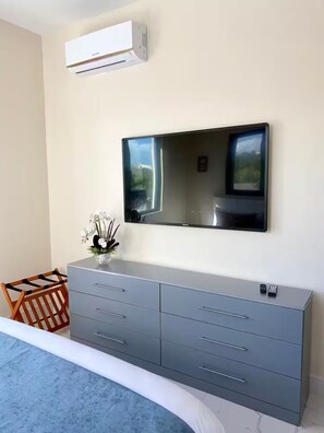 A bedroom with a bed, a grey dresser, a flat-screen TV mounted on the wall, and a white air conditioning unit above the dresser. - Grace Bay Hideaway. 1 bedroom, central Grace Bay. (Grace Bay)