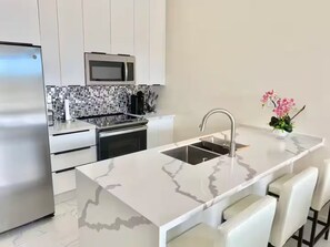 A modern kitchen with a central island, stainless steel appliances, and a tiled backsplash. - Grace Bay Hideaway. 1 bedroom, central Grace Bay. (Grace Bay)