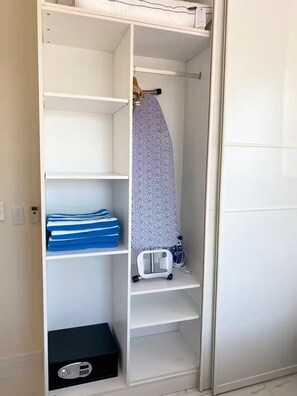 A white wardrobe with multiple shelves, a hanging rod, and a small black box on the bottom shelf. - Grace Bay Hideaway. 1 bedroom, central Grace Bay. (Grace Bay)
