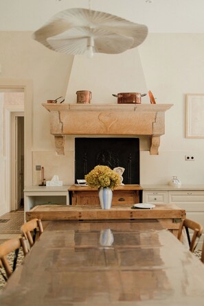 A dining area with a wooden table, chairs, a vase of flowers, a fireplace, and a hanging light fixture.