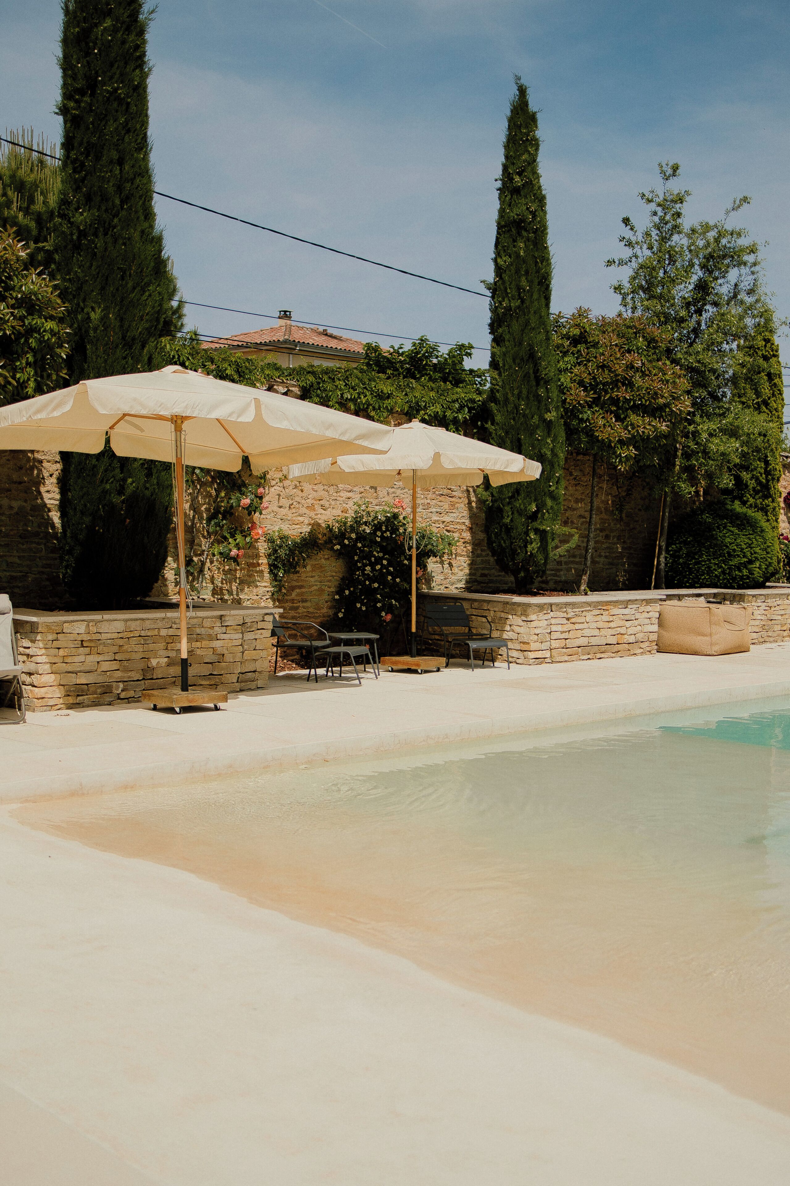Un espace piscine agrémenté de murs en pierre, de mobilier d’extérieur et de parasols.