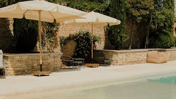 Un espace piscine agrémenté de murs en pierre, de mobilier d’extérieur et de parasols.