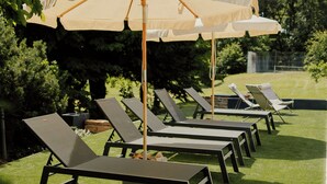 En rad solstolar med parasoller i en trädgårdsmiljö.