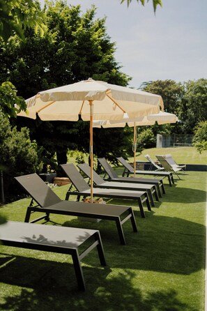 A row of lounge chairs with umbrellas in a garden setting.