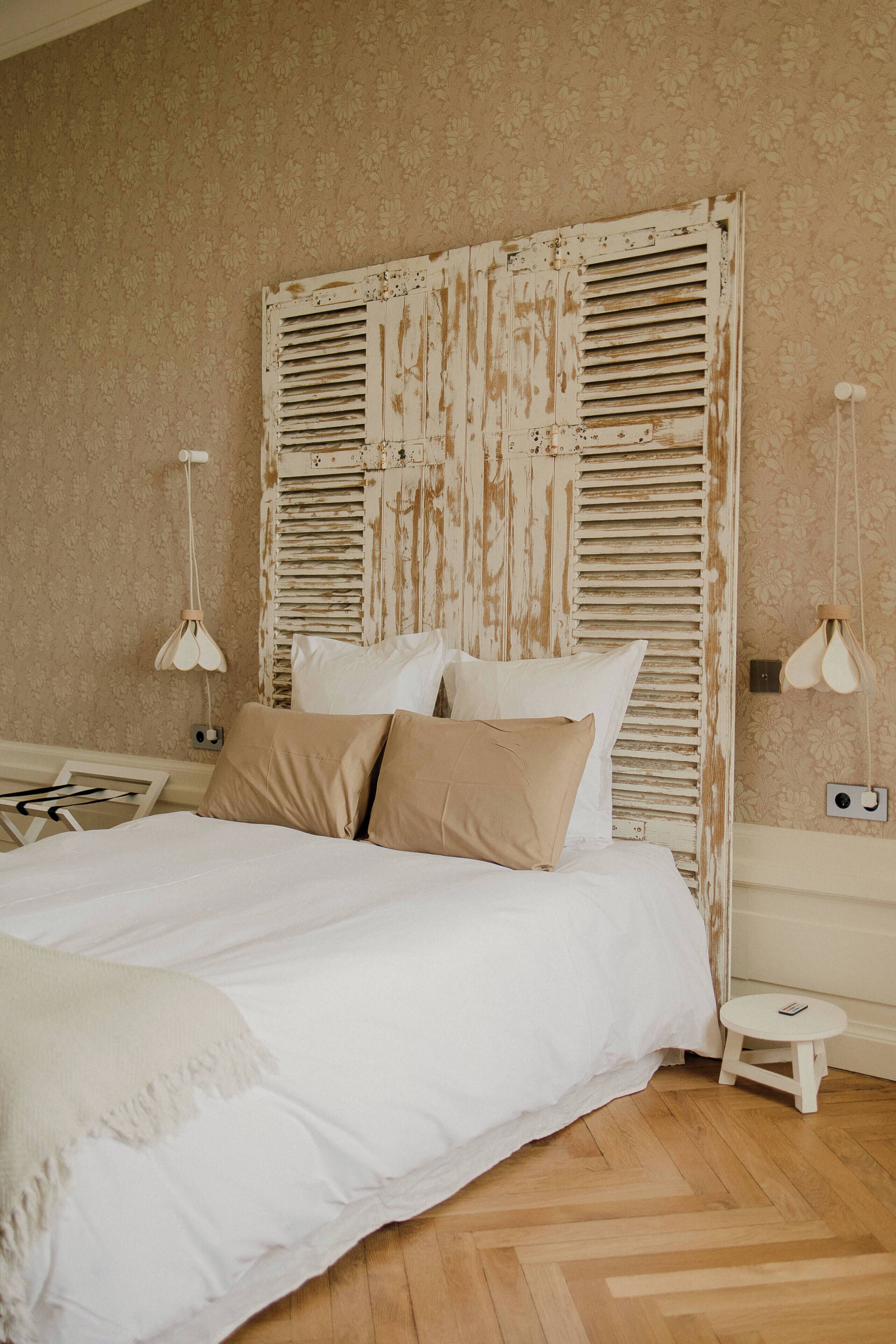 Een slaapkamer met een groot bed, een houten hoofdbord, twee bedlampen en een klein nachtkastje.