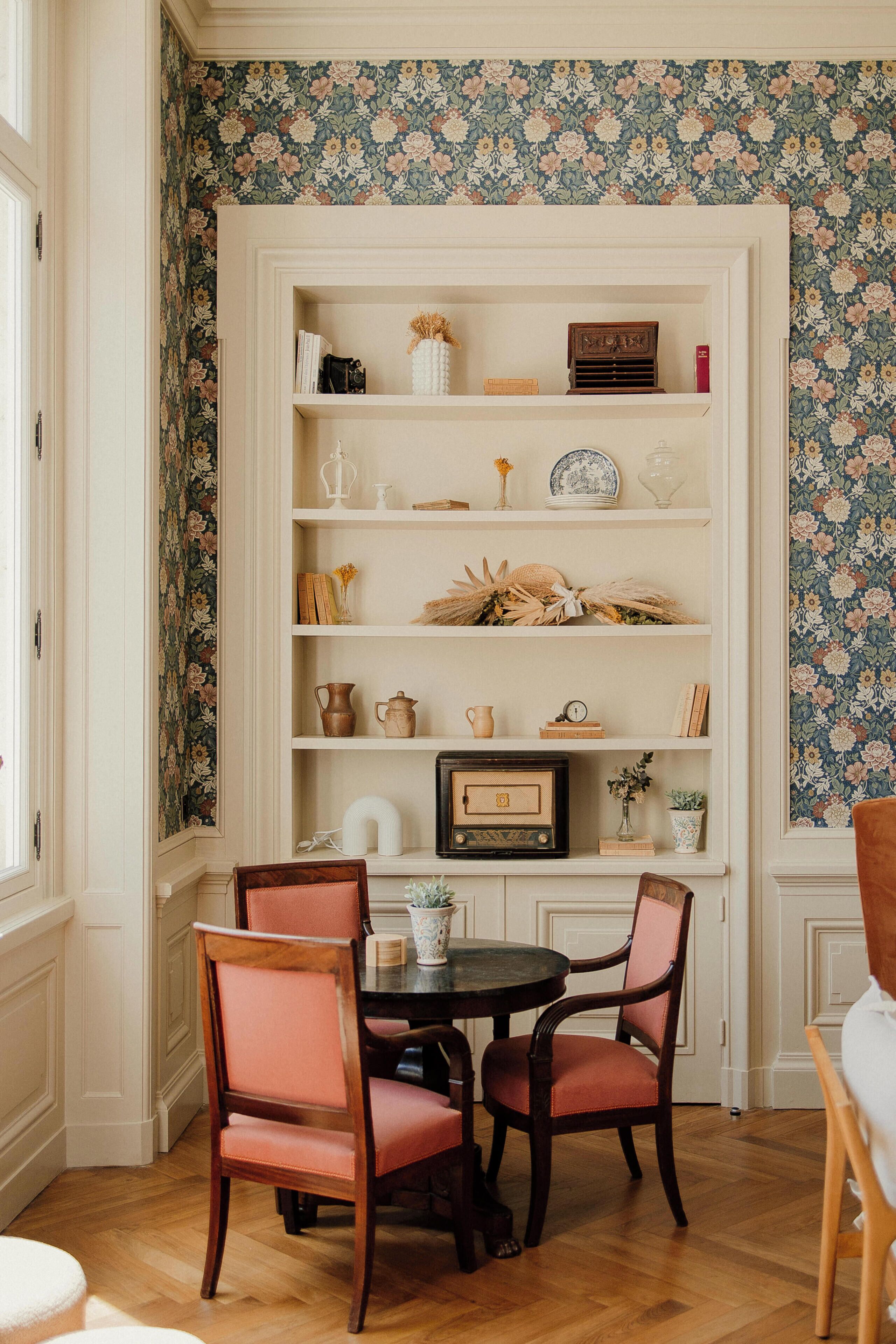 Comedor con mesa y sillas de madera, rodeado por un estante blanco con diversos objetos decorativos.