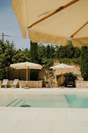 A swimming pool area with lounge chairs and umbrellas.