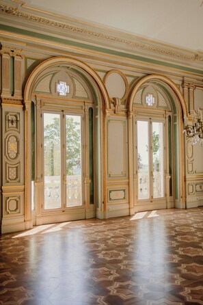 A spacious room with ornate moldings, large windows, and a patterned floor.