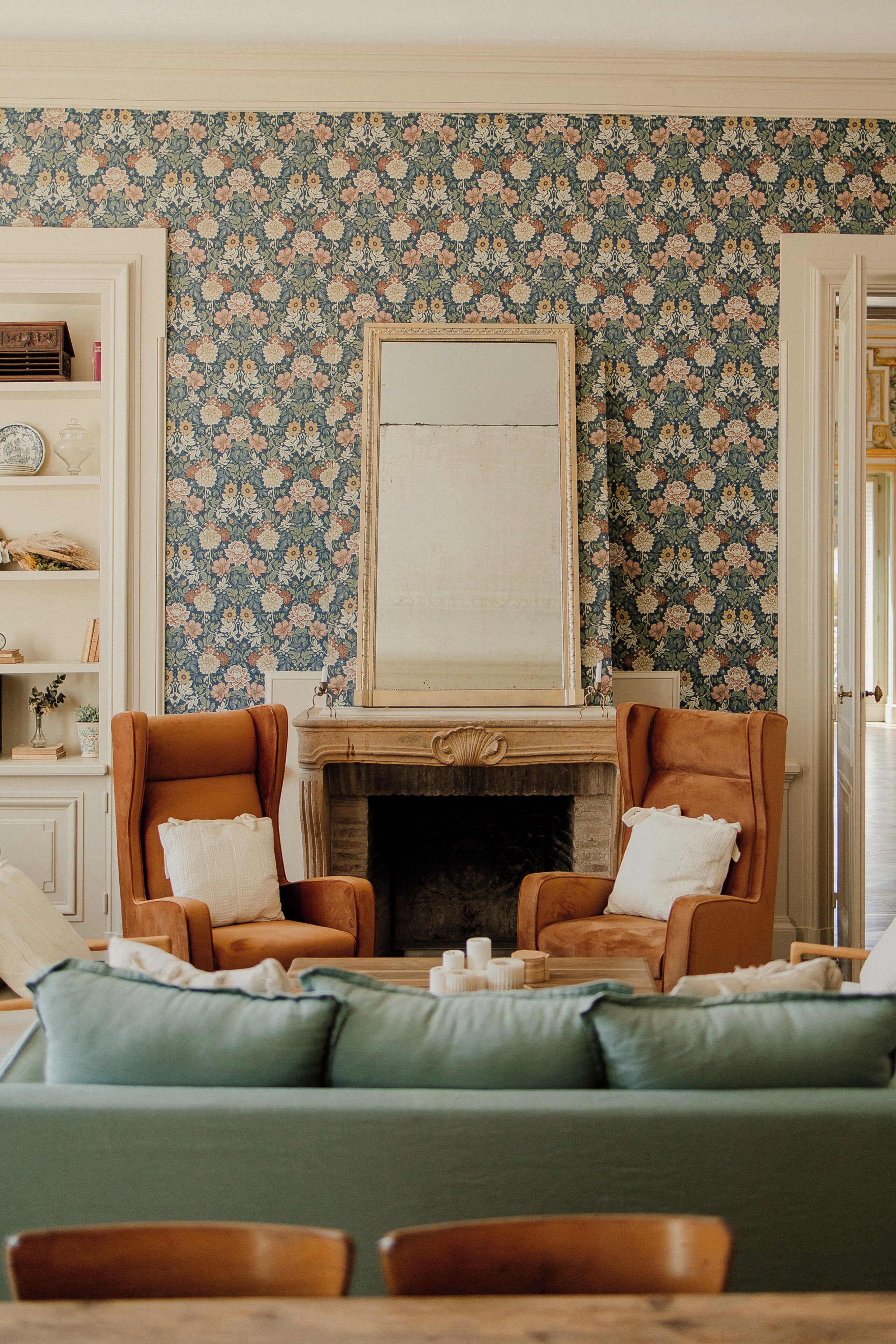 Een woonkamer met een open haard, twee fauteuils, een bank en een boekenkast.