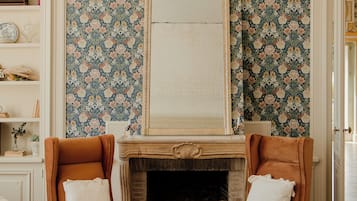 Een woonkamer met een open haard, twee fauteuils, een bank en een boekenkast.