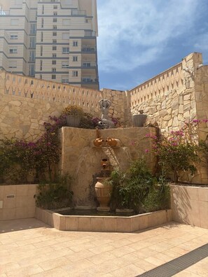 A courtyard with a fountain, stone wall, and potted plants. - EL RINCÓN DEL MAR APARTMENT (Calpe)