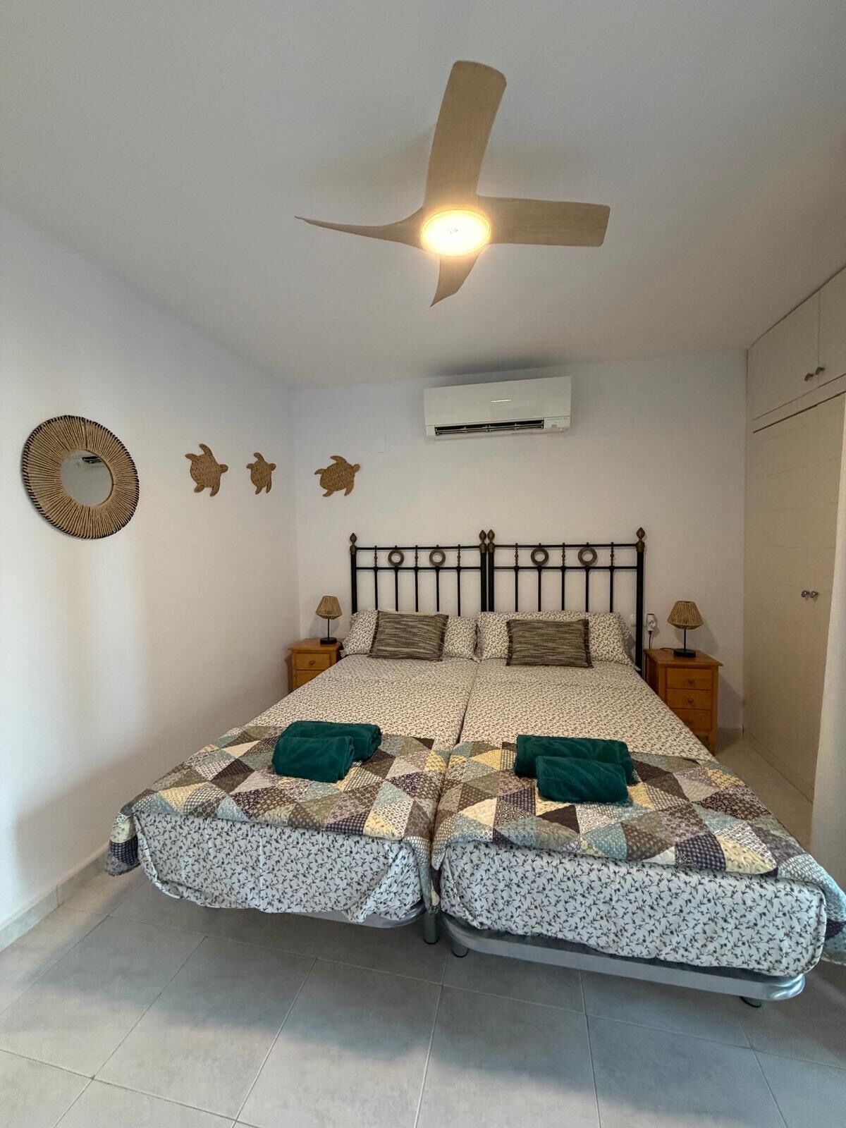 A bedroom with a bed, two nightstands, a ceiling fan, an air conditioning unit, and wall decorations.