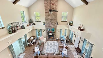 A spacious living area with a high ceiling, a fireplace, and a television.